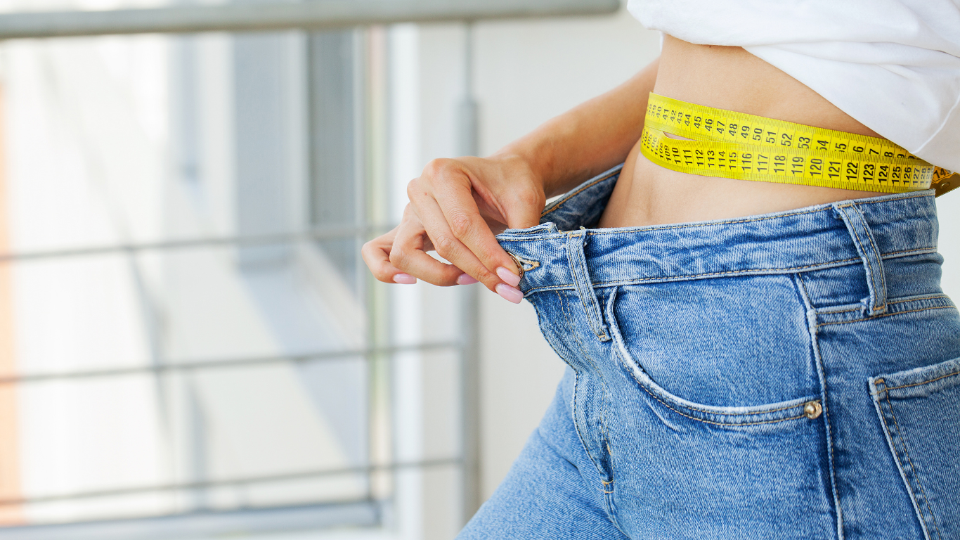 Close-up image of a person measuring their waist with a yellow tape measure, symbolizing weight loss progress.