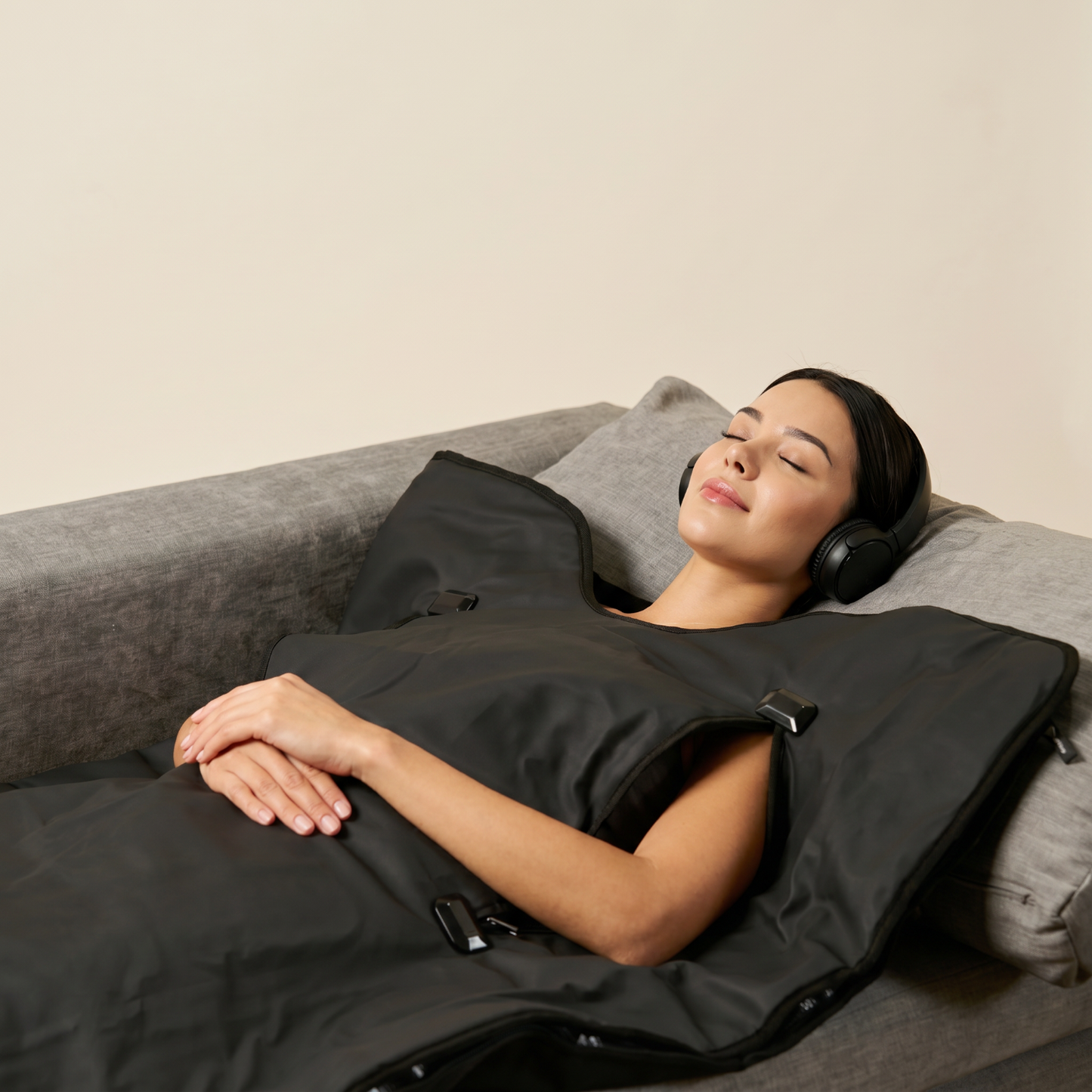 Woman lying on a couch with a black hooded blanket and headphones, possibly in a spa or relaxation setting.