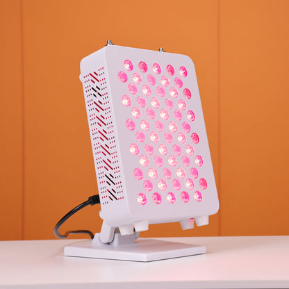 Angled side view of a Nicebeam red light therapy panel featuring 60 glowing LED lights, a vented design for heat dissipation, and an adjustable stand, set against a vibrant orange background.