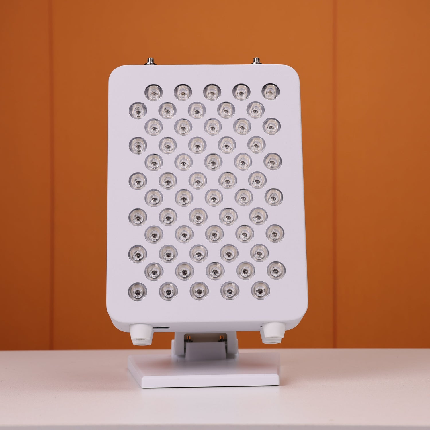 Front view of a Nicebeam red light therapy panel with 60 unlit LED lenses, showcasing its sleek design and even distribution, mounted on a stable adjustable stand, and set against a vibrant orange background.