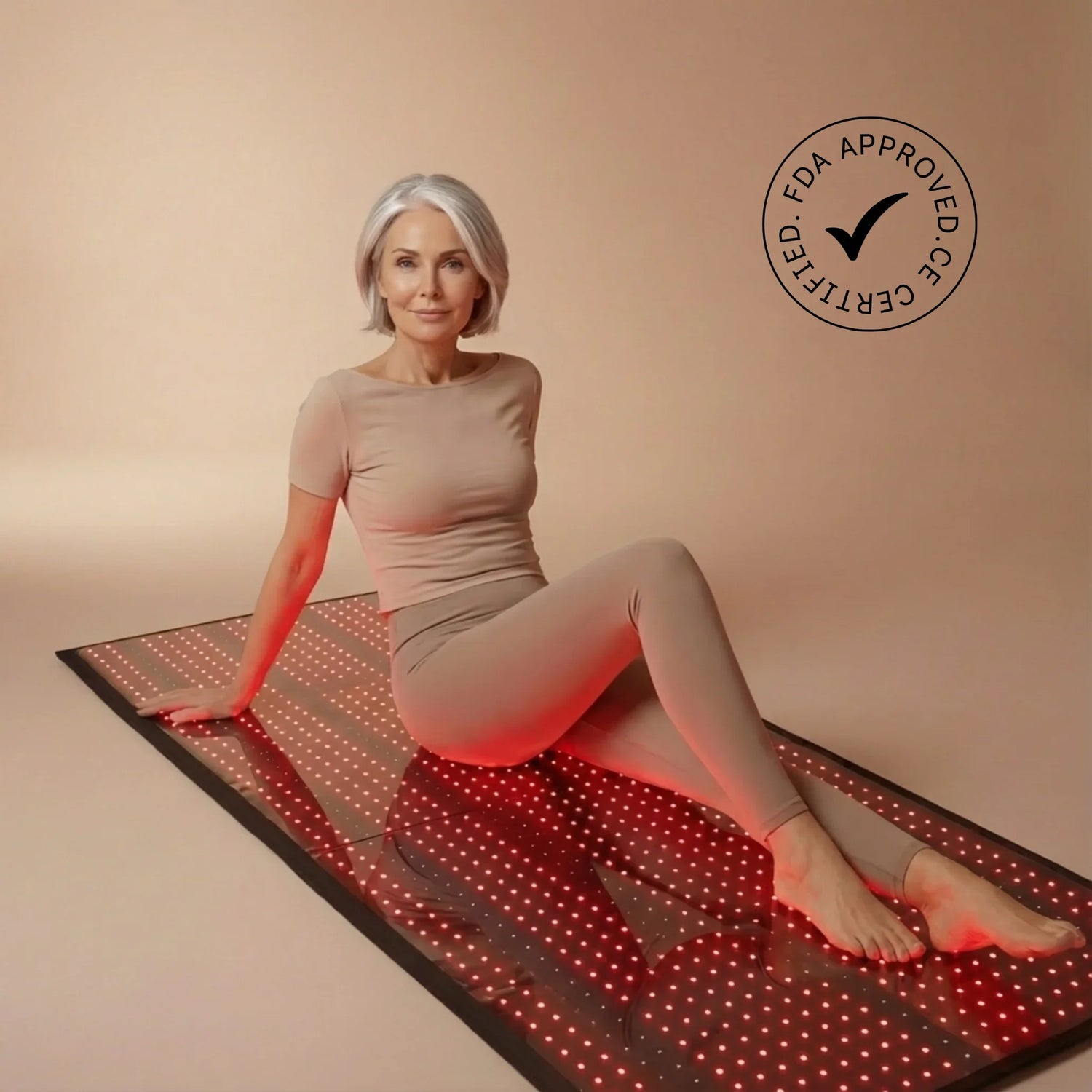 Woman sitting on a large red light therapy mat, FDA approved certification visible.