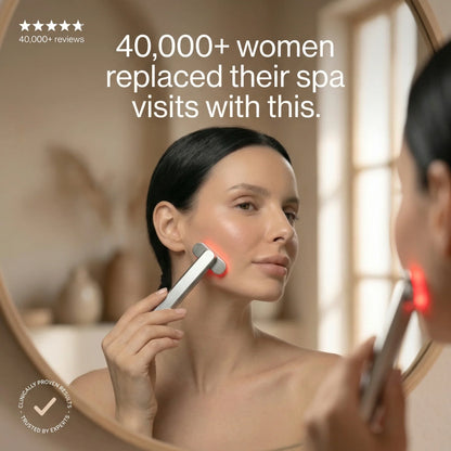 Woman using handheld red light therapy device on face in front of mirror, wellness skincare