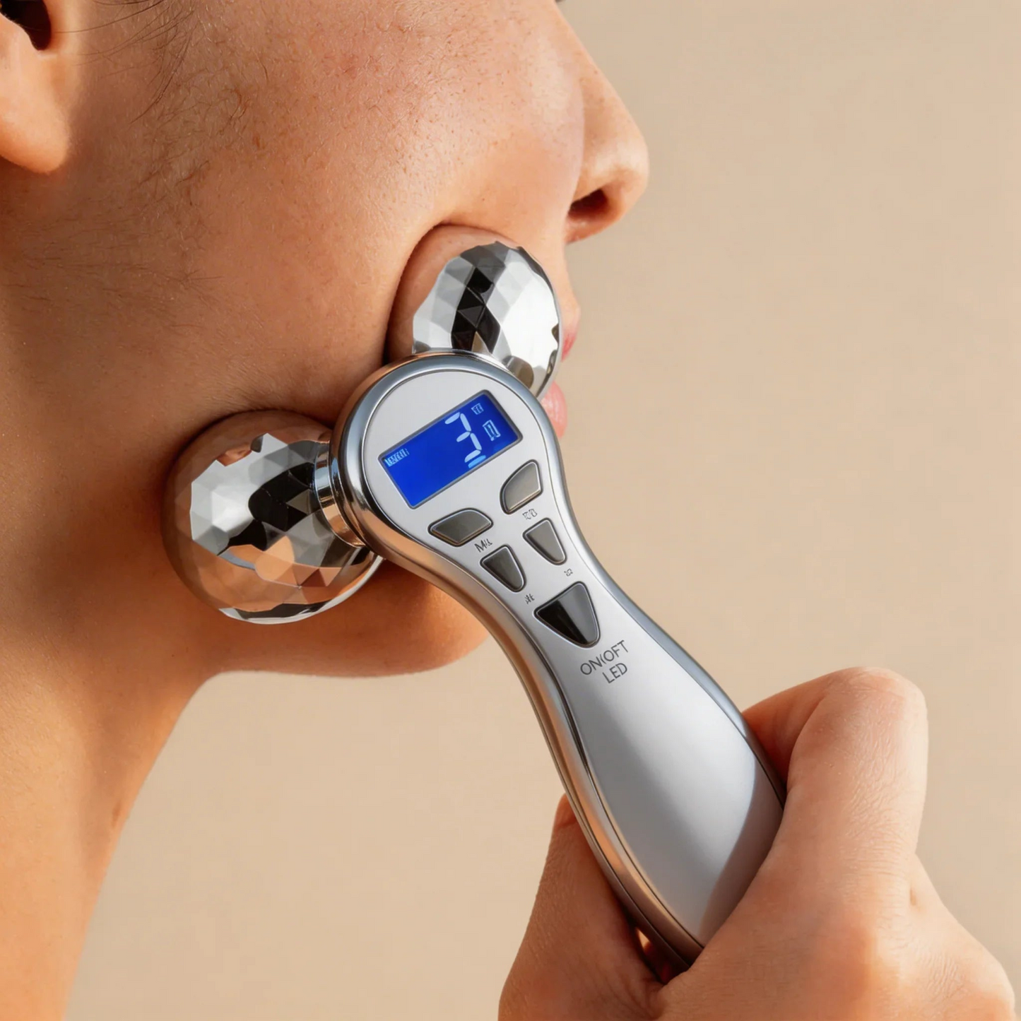 Person using a digital facial massager on their face with a beige background