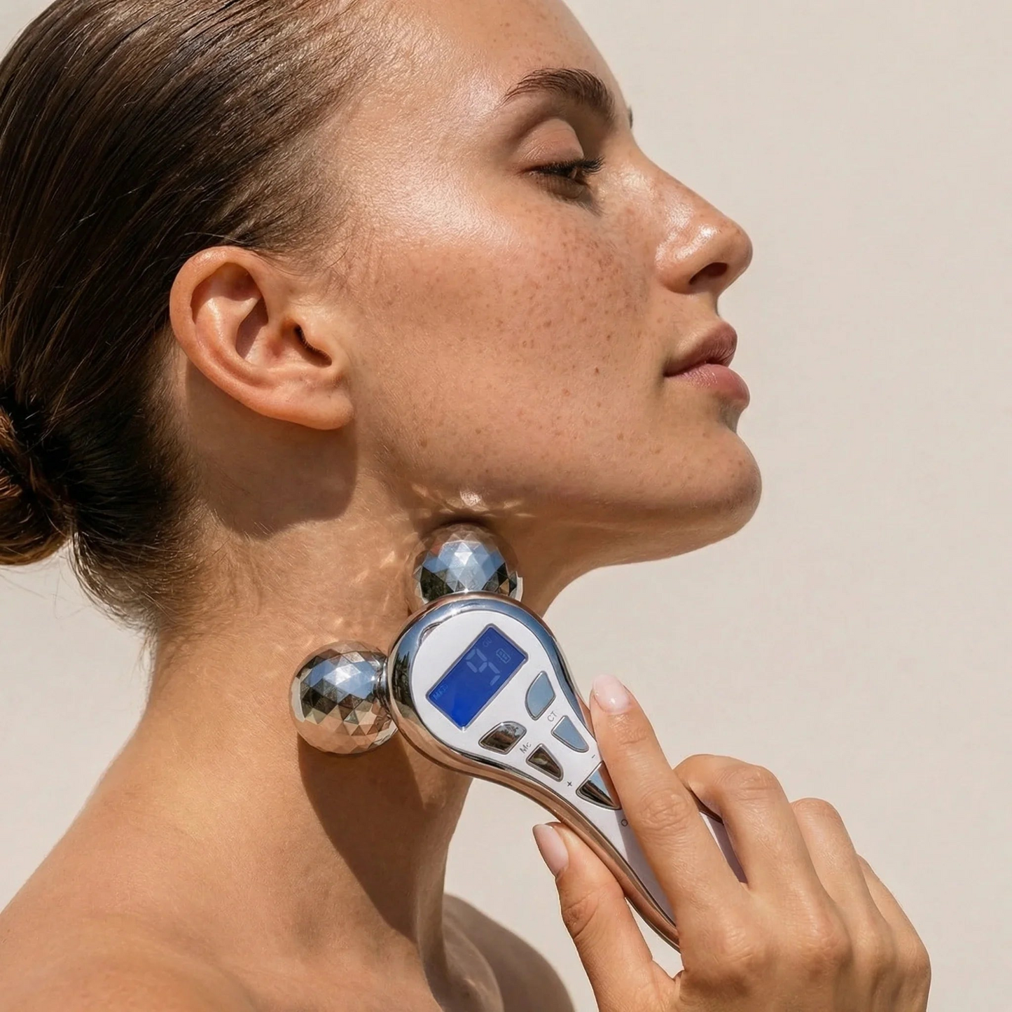 Woman using a handheld electronic device on her neck against a beige background