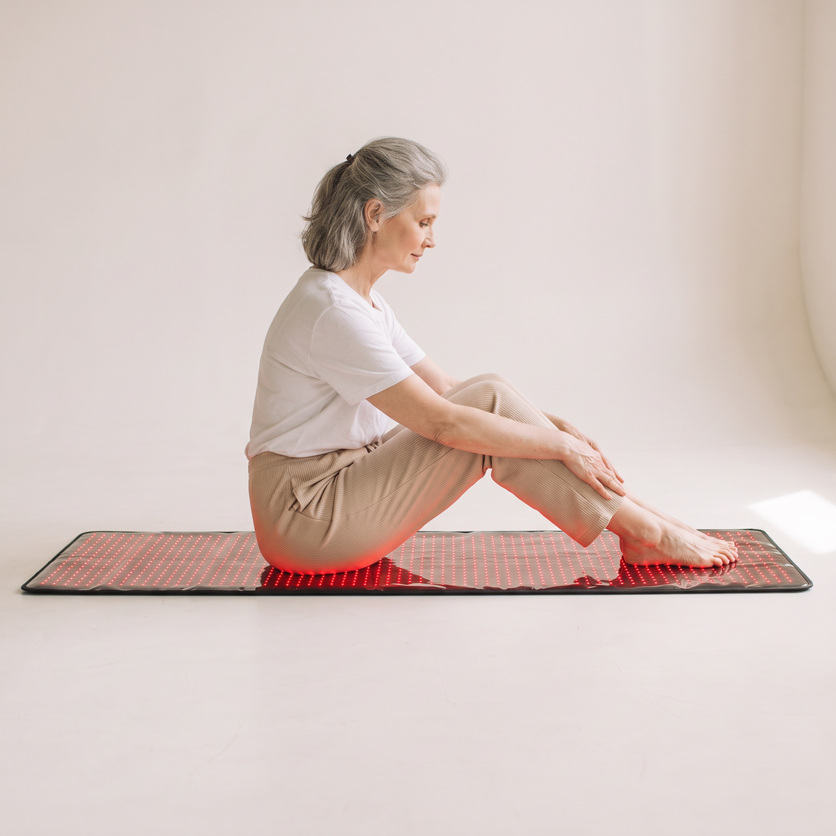 Woman sitting on the Nicebeam 63 inch red light therapy mat on the floor