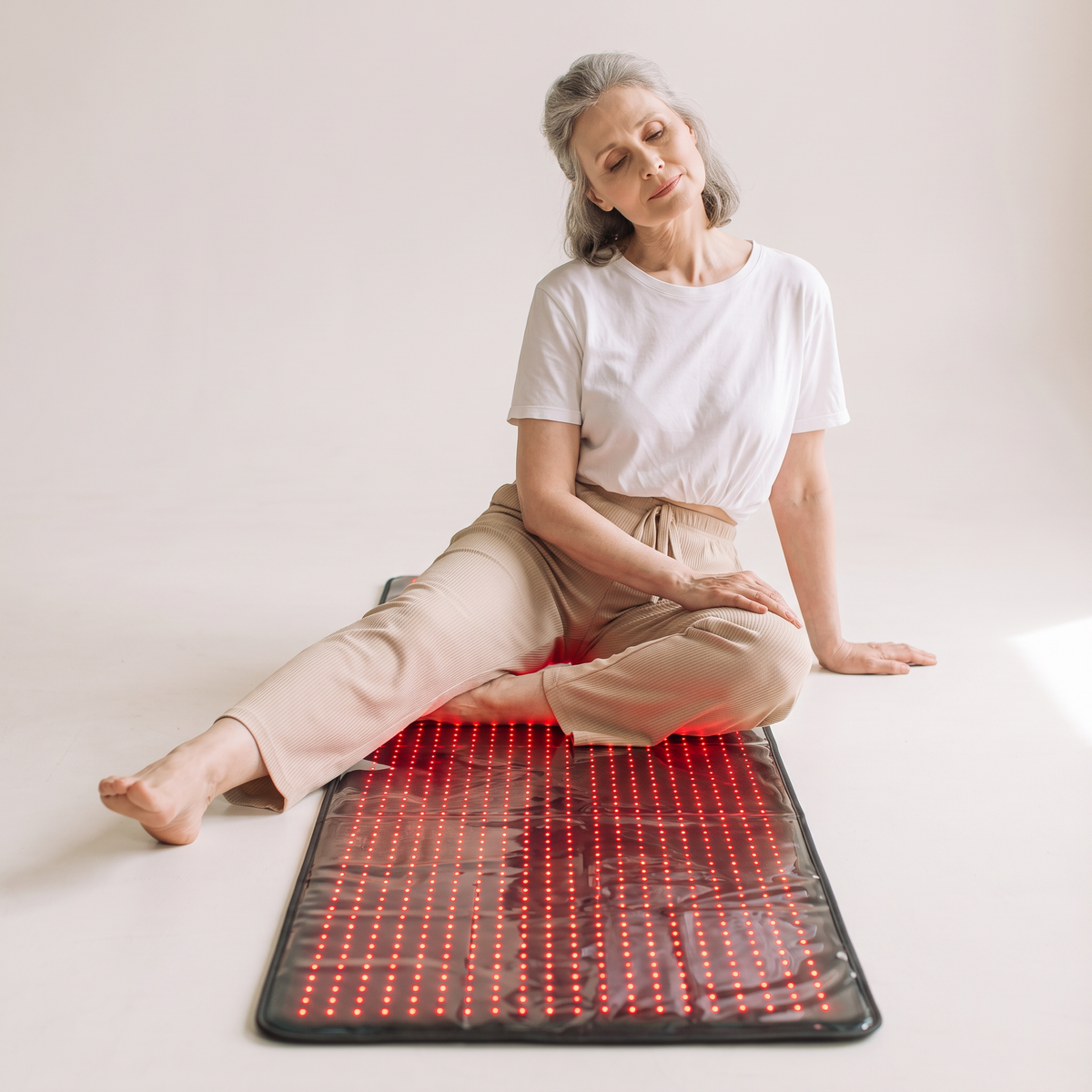 Woman in her 50s sitting on the Nicebeam 63 inch red light therapy mat at home