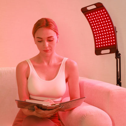 Woman sitting comfortably with a red light therapy lamp, illustrating its benefits for relaxation, pain relief, and energy boosting.