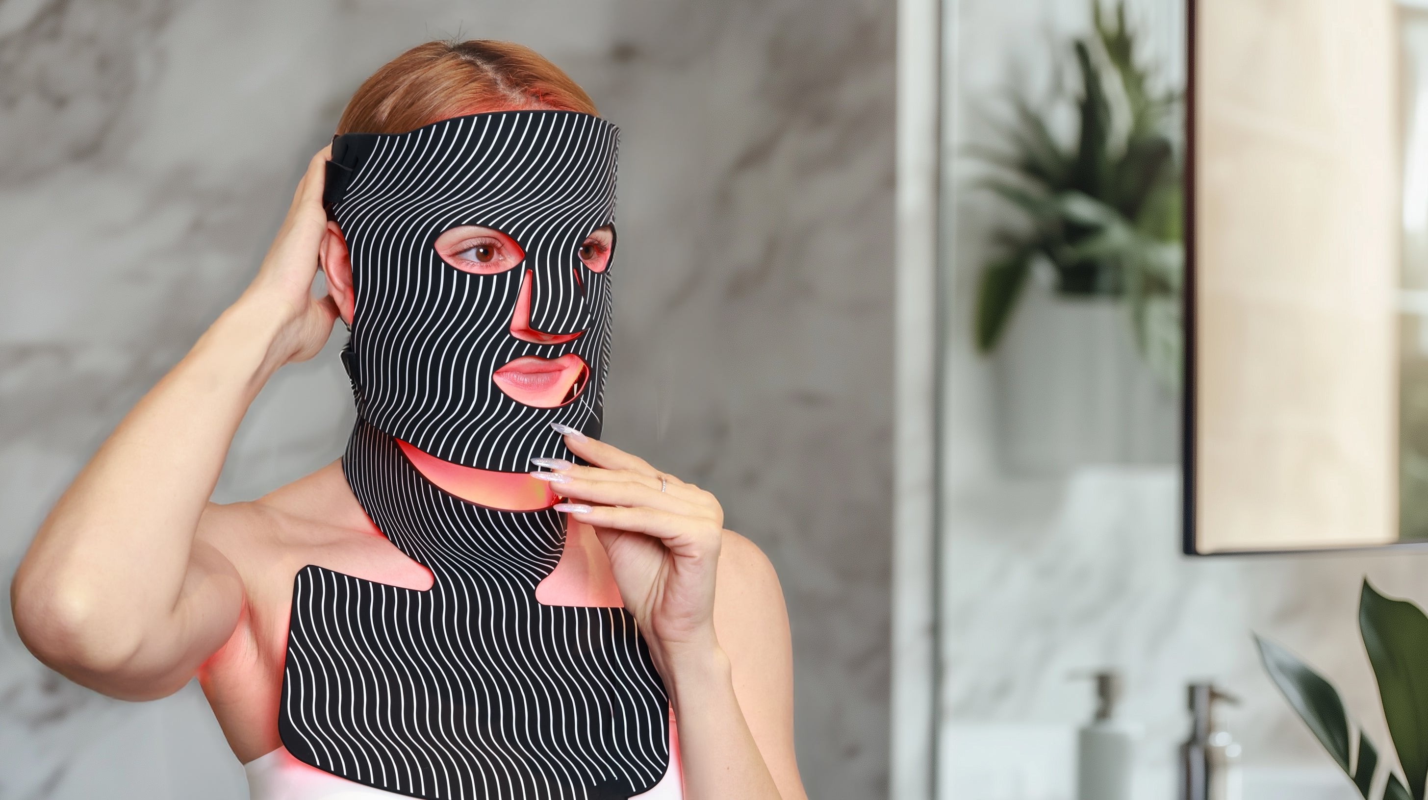 A woman is using a red light therapy mask as part of her night routine and for anti-aging purposes. However, this mask includes 7 different colors to address various skin issues.