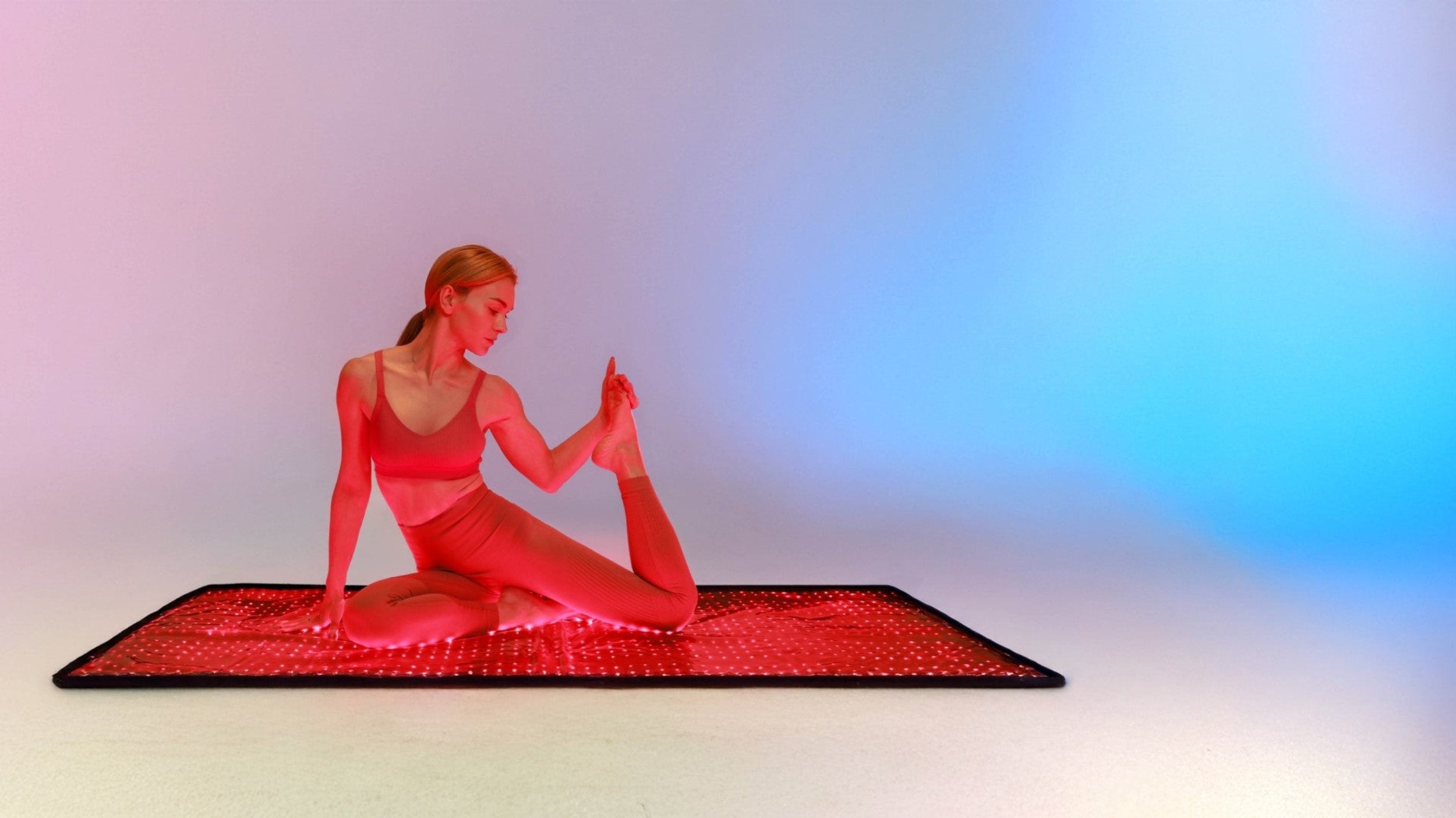 Woman performing a yoga stretch on a red light therapy mat, showcasing its benefits for fitness and wellness.